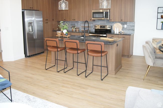 Kitchen with stainless steel appliances, a sink, brown cabinetry, tasteful backsplash, and a breakfast bar area | Image 4