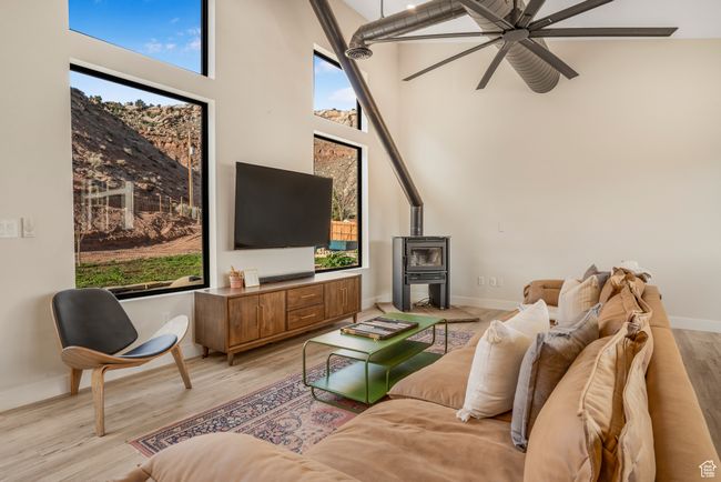 Living room with a wood stove, ceiling fan, a towering ceiling, light wood finished floors, and baseboards | Image 16