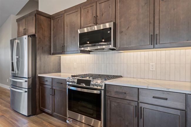 Kitchen featuring appliances with stainless steel finishes, dark wood finished floors, backsplash, dark brown cabinetry, and lofted ceiling | Image 18