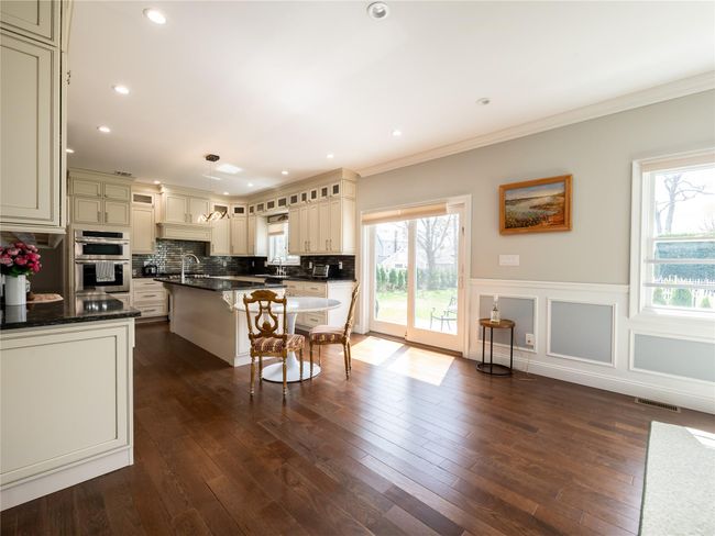 Kitchen featuring stainless steel double oven, a breakfast bar area, a wainscoted wall, ornamental molding, and a kitchen island | Image 7