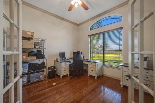 The designated study features glass French doors, wood flooring, crown molding, a ceiling fan and sits at the front of the house | Image 4