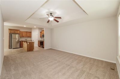 Unfurnished living room featuring ceiling fan, a raised ceiling, and light carpet | Image 3