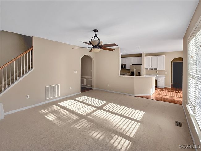 Unfurnished living room featuring arched walkways, light carpet, ceiling fan, and stairway | Image 8