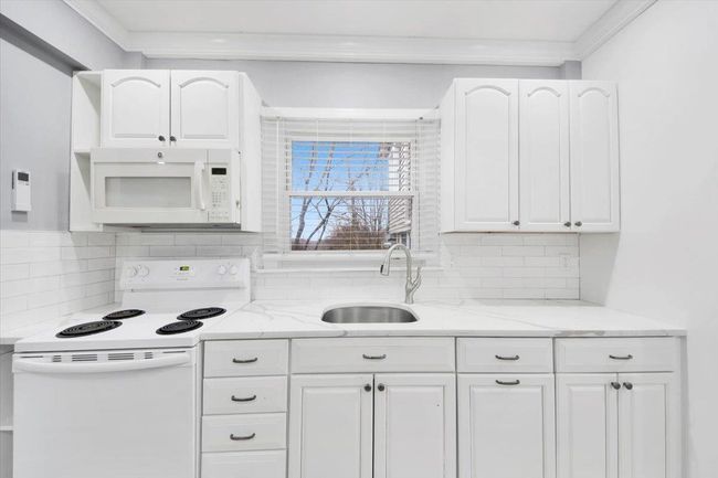 Kitchen with white appliances, a sink, white cabinetry, backsplash, and light stone counters | Image 9