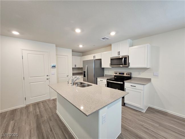 Kitchen with appliances with stainless steel finishes, a sink, wood finished floors, a center island with sink, and white cabinetry | Image 9