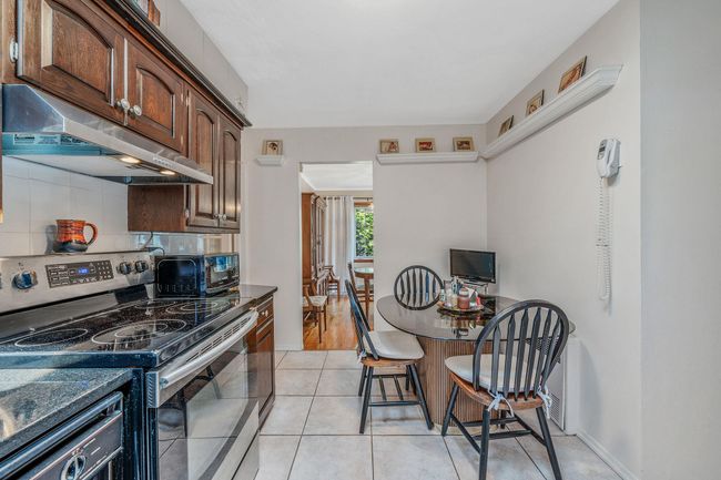 Kitchen featuring electric stove, range hood, backsplash, light tile patterned flooring, and dark brown cabinetry | Image 10