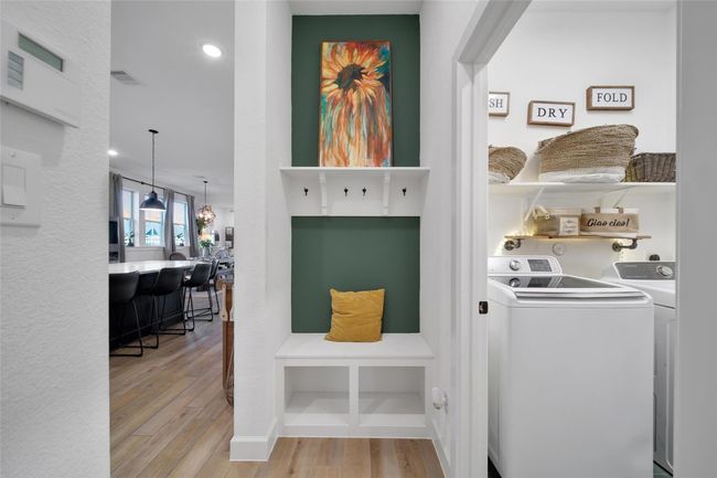 This photo showcases a modern, open-concept interior with a cozy entry nook featuring a bench and vibrant artwork. Adjacent is a stylish laundry room with organized shelving. The space exudes warmth with wooden floors and contemporary lighting. | Image 38