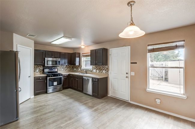 Kitchen with stainless steel appliances, backsplash, light countertops, light wood finished floors, and a textured ceiling | Image 7