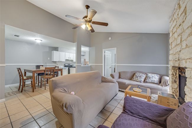 Unit B Living room with ceiling fan, light tile patterned floors, lofted ceiling, and a stone fireplace | Image 20