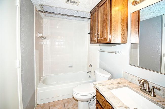 Full bathroom with a textured ceiling, washtub / shower combination, tile patterned floors, vanity, and toilet | Image 25