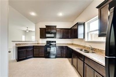 Kitchen with light tile, black stove, sink, and dark brown cabinetry - picture when they purchased 2018 | Image 2