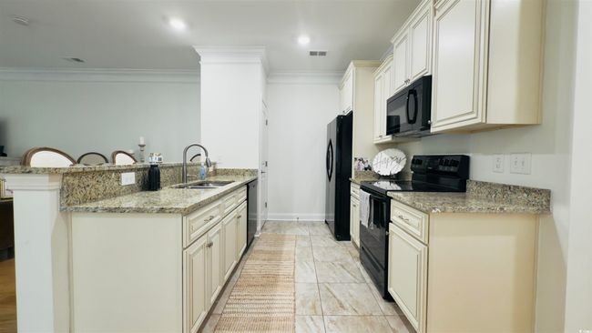 Kitchen featuring black appliances, crown molding, a peninsula, light stone counters, and a kitchen bar | Image 13