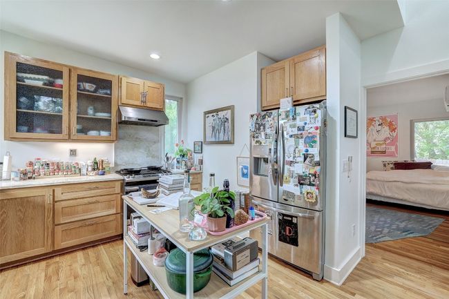 Kitchen featuring light brown cabinetry, under cabinet range hood, glass insert cabinets, light wood-style flooring, and stainless steel refrigerator with ice dispenser | Image 37