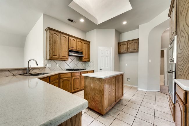 Kitchen with arched walkways, backsplash, under cabinet range hood, stainless steel appliances, and brown cabinets | Image 13