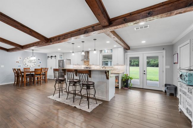 Kitchen with wall chimney range hood, a breakfast bar area, beamed ceiling, white cabinetry, and dark wood-style floors | Image 10