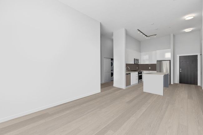 Kitchen featuring white cabinets, a towering ceiling, stacked washer / dryer, light countertops, and appliances with stainless steel finishes | Image 8