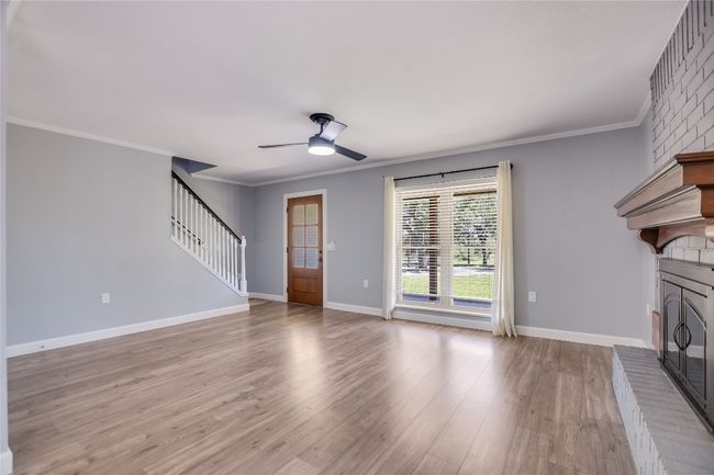Unfurnished living room with stairs, ceiling fan, wood finished floors, crown molding, and a brick fireplace | Image 7