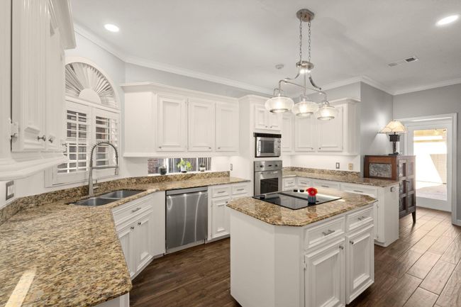 CHEF's KISS with this timeless white kitchen - bright and inviting, perfect for everyday living and entertaining. A spacious pantry includes a clever hidden storage area beneath the stairs for added functionality. And, recess lighting, a new pendant over the island, and peek-a-boo windows along the counters offer beautiful light. | Image 15