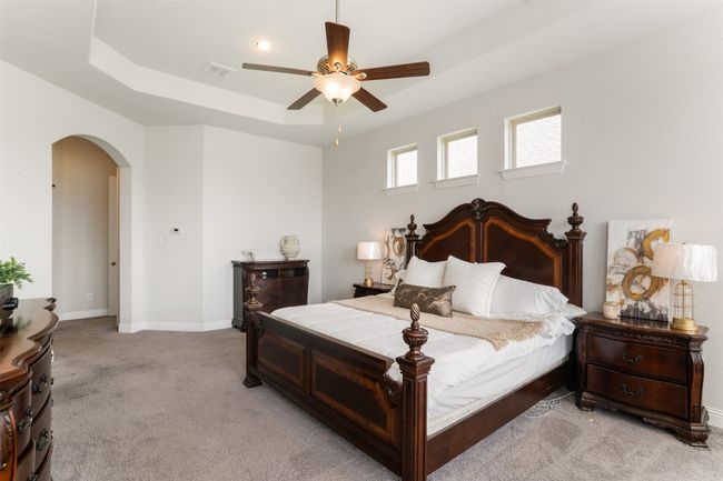 Bedroom with light carpet, a tray ceiling, arched walkways, baseboards, and visible vents | Image 22