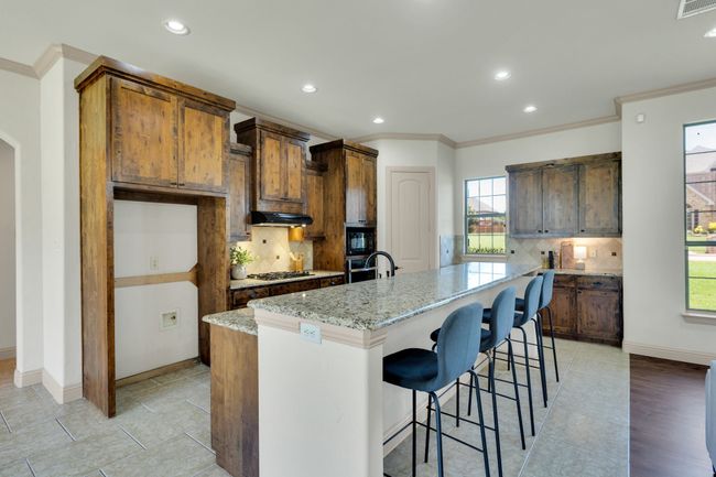Kitchen featuring crown molding, backsplash, recessed lighting, an island with sink, and light stone counters | Image 10