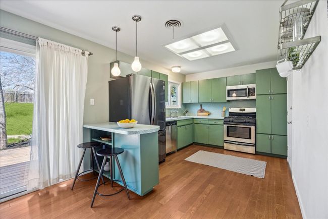 Kitchen with wood finished floors, green cabinetry, a peninsula, a sink, and appliances with stainless steel finishes | Image 8