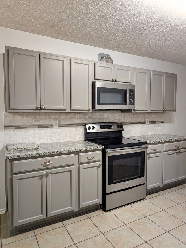 Kitchen featuring stainless steel appliances, gray cabinets, a textured ceiling, backsplash, and light tile patterned flooring | Image 6
