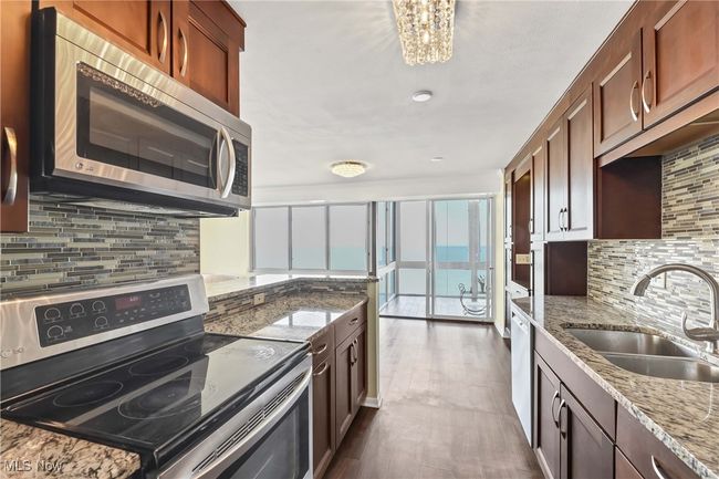 Kitchen with light stone countertops, a sink, stainless steel appliances, a notable chandelier, and tasteful backsplash | Image 13