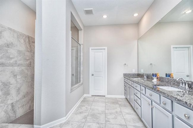 bathroom features a spacious layout with a large walk-in shower, dual sink vanity with granite countertops, ample storage, and elegant tile flooring. | Image 18