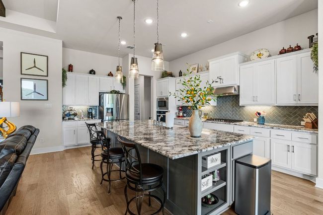 Kitchen with white cabinets, an island with sink, appliances with stainless steel finishes, hanging light fixtures, and under cabinet range hood | Image 14