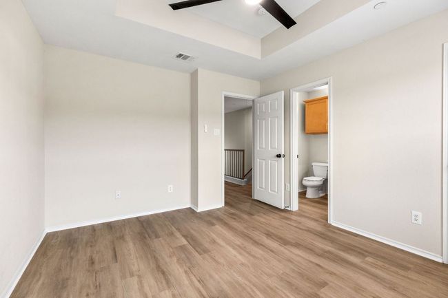 Unfurnished bedroom featuring light wood finished floors, a raised ceiling, visible vents, ensuite bath, and baseboards | Image 24