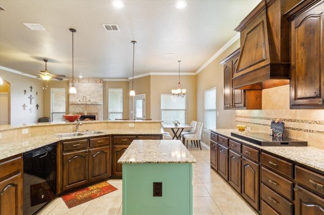Kitchen with backsplash, a center island, custom range hood, black appliances, and a sink | Image 18