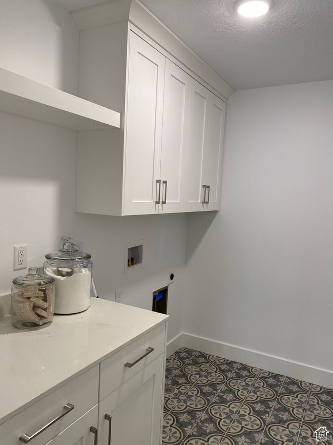 Laundry area featuring hookup for a washing machine, a textured ceiling, electric dryer hookup, cabinet space, and baseboards | Image 14