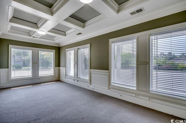 Empty room with coffered ceiling, a wainscoted wall, carpet flooring, beam ceiling, and ornamental molding | Image 12