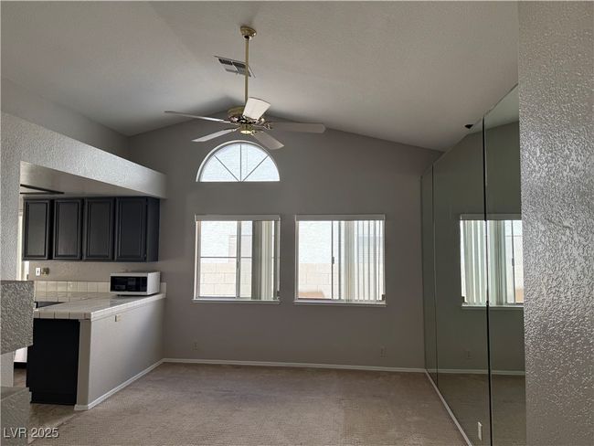 Kitchen with tile counters, white microwave, vaulted ceiling, a ceiling fan, and light carpet | Image 5