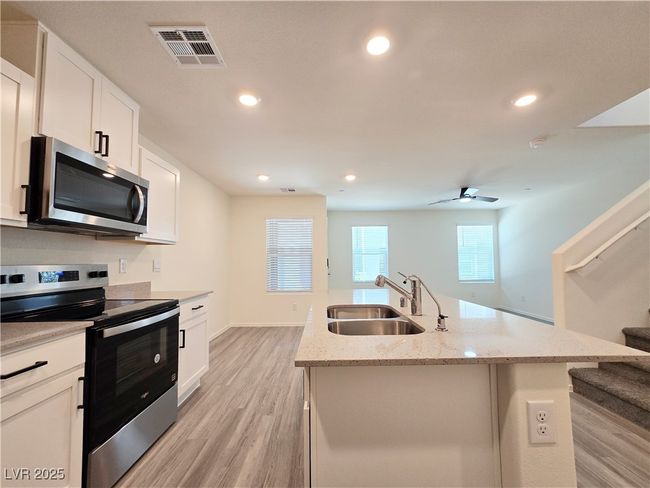 Kitchen featuring stainless steel appliances, a sink, light wood-type flooring, an island with sink, and white cabinetry | Image 12