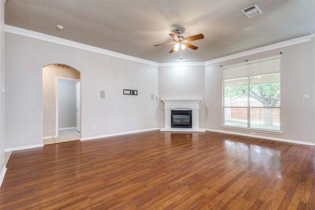 Unfurnished living room with ceiling fan, arched walkways, wood finished floors, a glass covered fireplace, and crown molding | Image 6