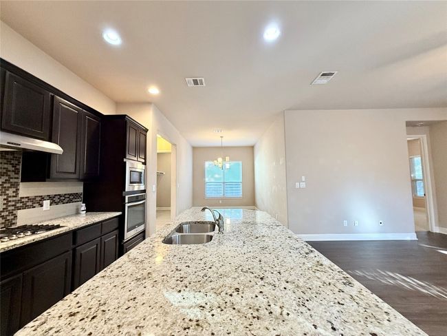 Kitchen with a chandelier, tasteful backsplash, light stone countertops, dark wood-style flooring, and recessed lighting | Image 17
