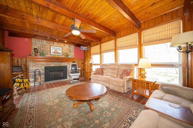 Living area featuring beamed ceiling, a fireplace, a ceiling fan, and wood ceiling. | Image 14