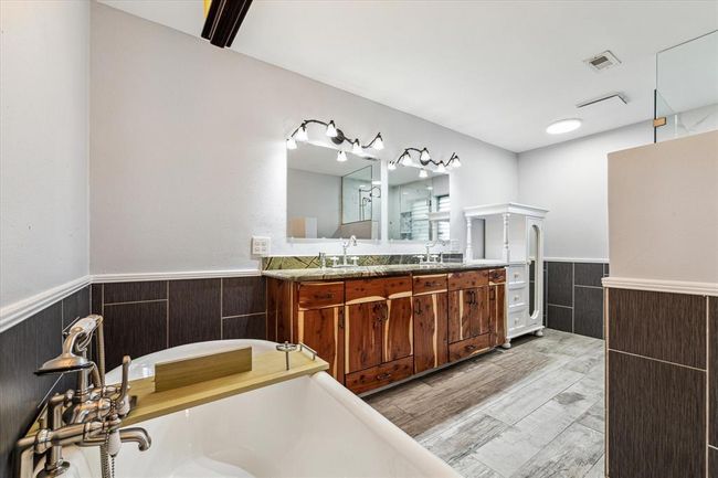 A spacious, updated primary ensuite bathroom with a standalone soaking tub and a double vanity, along with tile flooring and a tile wall surround, creates a sleek and modern aesthetic | Image 9