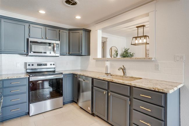 Kitchen featuring stainless steel appliances, ornamental molding, a sink, decorative backsplash, and light tile patterned flooring | Image 15
