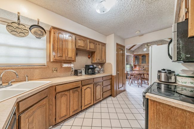 Kitchen with light tile patterned floors, range with electric stovetop, light countertops, a ceiling fan, and a textured ceiling | Image 11