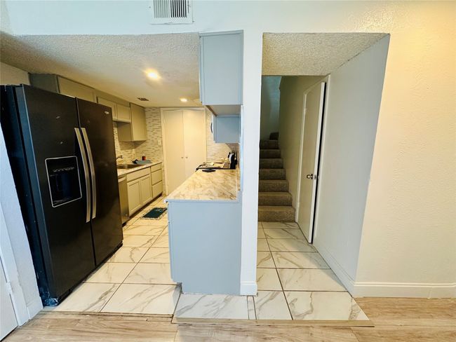 Kitchen with black refrigerator with ice dispenser, light countertops, backsplash, a textured ceiling, and baseboards | Image 7