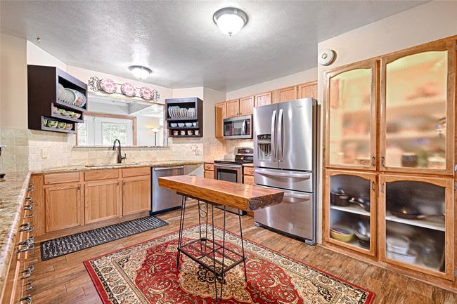 Kitchen with backsplash, sink, light hardwood / wood-style flooring, light stone counters, and stainless steel appliances | Image 17