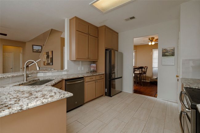 Kitchen with light stone counters, a sink, a ceiling fan, appliances with stainless steel finishes, and visible vents | Image 13