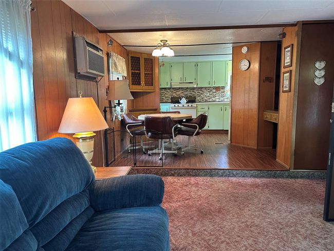 Living area featuring an AC wall unit, dark carpet, wooden walls, and dark wood-type flooring | Image 6