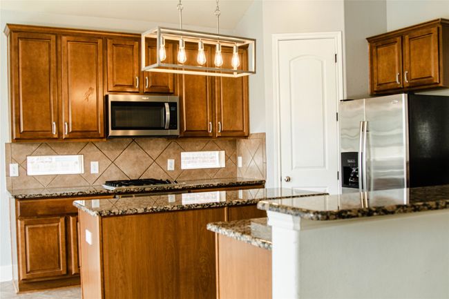 Kitchen with stainless steel appliances, dark stone countertops, decorative backsplash, and brown cabinets | Image 10