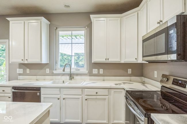 kitchen featuring stainless steel appliances, healthy amount of natural light, white cabinetry, and light stone countertops | Image 11