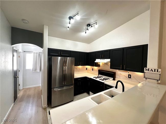 Kitchen featuring freestanding refrigerator, dark cabinetry, a sink, and under cabinet range hood | Image 8