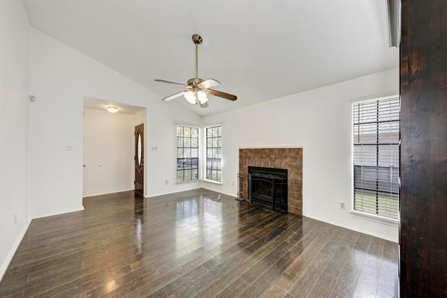 Unfurnished living room featuring baseboards, ceiling fan, vaulted ceiling, a tile fireplace, and dark wood-style flooring | Image 8