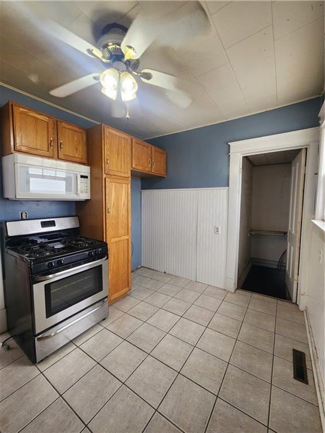 Kitchen with light tile patterned floors, a wainscoted wall, ceiling fan, and range | Image 24